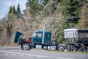 Broken big rig semi truck with an open hood and loaded semi trai