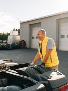 A worker smearing trailer fifth wheel coupling with lubricant oil. Semi-truck mechanical maintenance