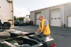 A worker smearing trailer fifth wheel coupling with lubricant oil. Semi-truck mechanical maintenance